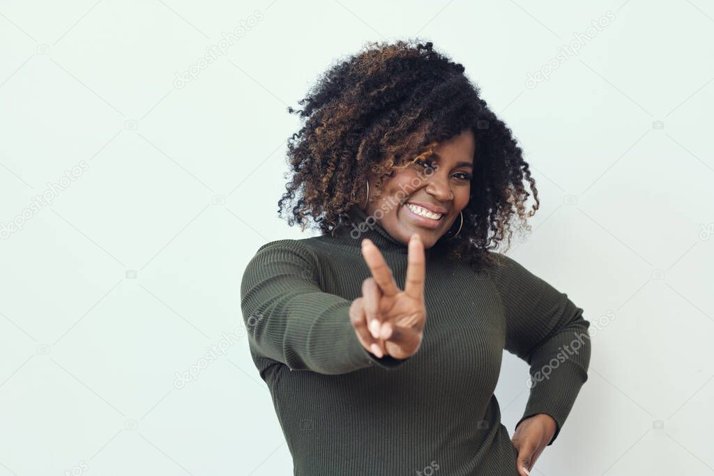 Portrait of happy Afro woman with frizzy hair showing peace sign against white background