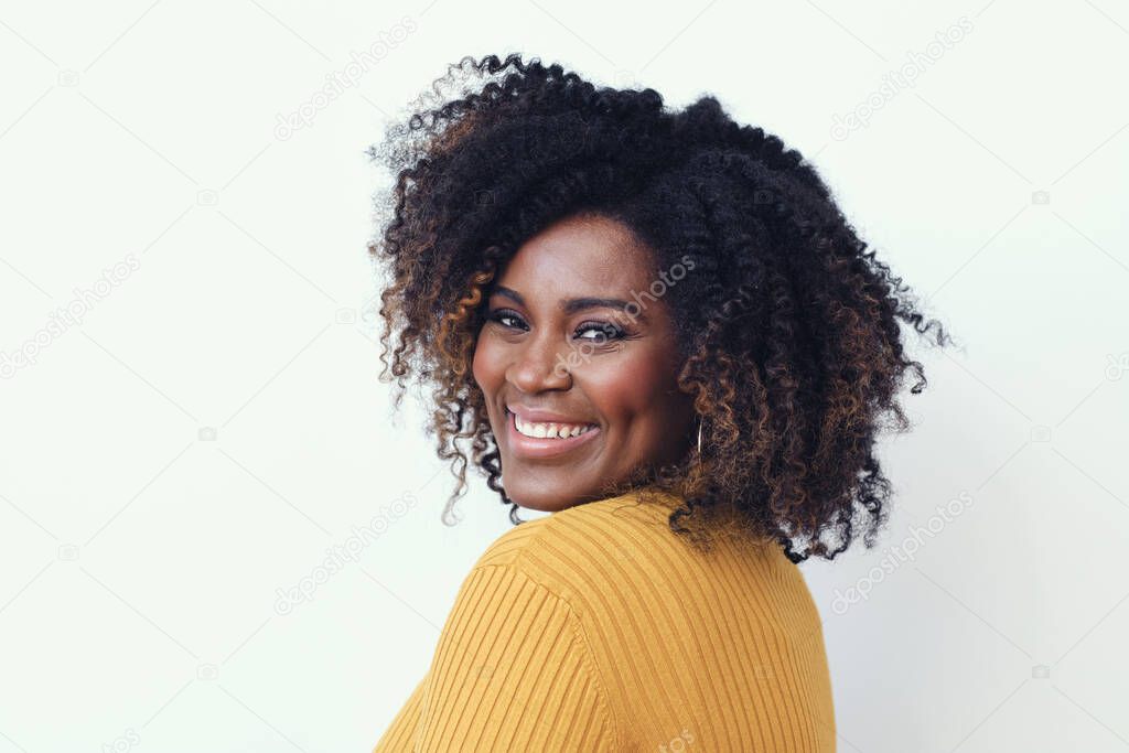 Portrait of happy beautiful young woman with curly hair wearing yellow sweater against white background