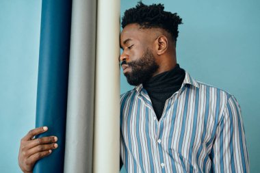 Gözü mavi gömlekli Afro-Amerikan bir adamın portresi. Kopya alanı olan duvarın yanında dikilirken gözlerini kaçırıyor.