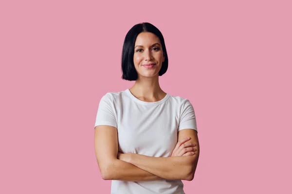 Pembe arka planda kollarını kavuşturmuş güzel bir genç kadının portresi.