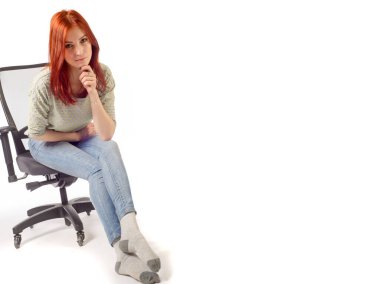 Ofis koltuğunda oturan, kot pantolonlu kızıl saçlı kız.