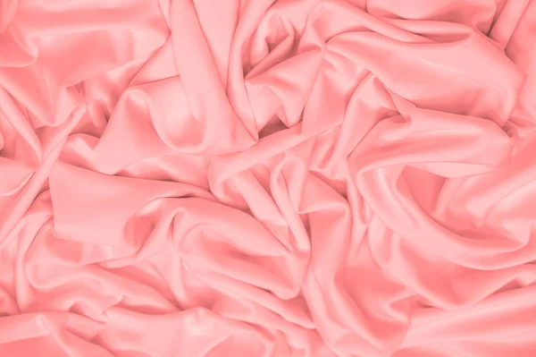 The fabric is silk of a pale red color. Texture. Background. Pattern. Silk fabric has a shiny sheen and characteristic small folds that run horizontally. She lies down in soft folds