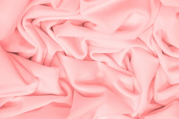 The fabric is silk of a pale red color. Texture. Background. Pattern. Silk fabric has a shiny sheen and characteristic small folds that run horizontally. She lies down in soft folds
