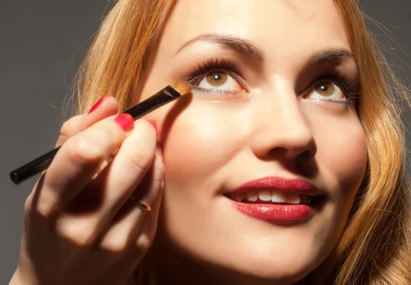 The girl with a brush for makeup. A beautiful young woman wearing red lipstick and biting a makeup brush