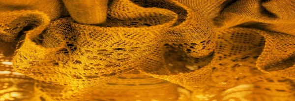 Yellow lace fabric, a thin open fabric, usually of cotton or silk, made using loops, twisting or knitting threads into patterns. Background texture, pattern.
