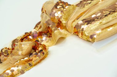 Çekirdekler altın rengidir. Kumaş dekorasyonu için kurdele. Arka plan dokusu, gün doğumu. İnce bir kumaş örgüsü üzerinde yuvarlak altın pulların pürüzsüz yamacı.