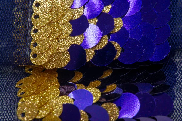 Sequins in blue, gold. Ribbon for fabric decoration. Background texture, sunrise. Smooth slope of rows of round blue, gold sequins on a thin mesh of fabric.