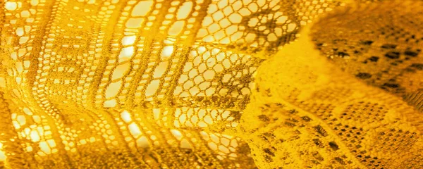 Yellow lace fabric, a thin open fabric, usually of cotton or silk, made using loops, twisting or knitting threads into patterns. Background texture, pattern.