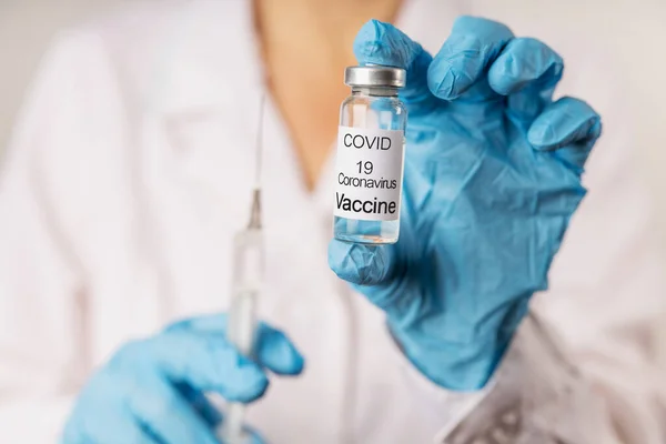 Vial with COVID-19 vaccine against coronavirus infection, in the hand of a doctor in a nitrile glove on a white background. Close-up. Fight against coronavirus concept