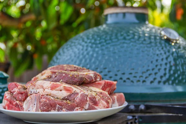 Carne cruda en un plato, cortada en trozos, sazonada y lista para asar, al aire libre, con el telón de fondo de una parrilla de barbacoa de cerámica llamada kamado o musikamado, una estufa japonesa. Primer plano, pequeña profundidad de — Foto de Stock