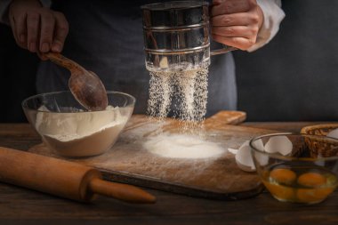 Women's hands, flour and dough. A woman, in an apron prepares dough for homemade baking, a rustic home cozy atmosphere, a dark background with unusual lighting.
