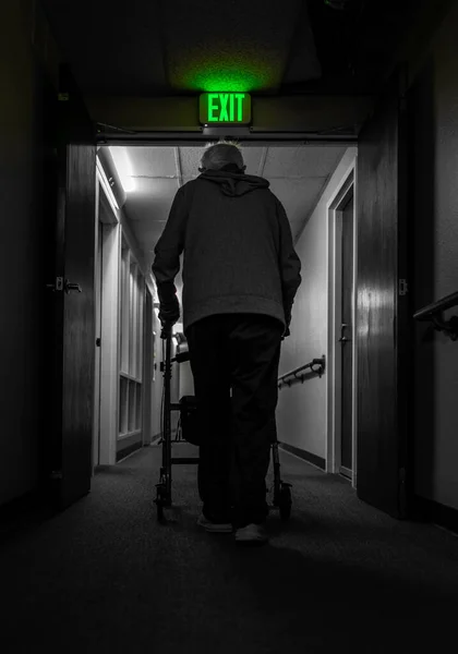 一个孤独的老人靠在人行道上 走在黑暗的走廊里 走在出口的标志下 社会援助 — 图库照片