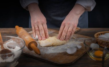 Kadın eli, un ve hamur. Ev yapımı pişirme hamuru pişiren önlüklü bir kadın. Ev yapımı, sade bir atmosfer. Sıradışı ışıklandırması olan karanlık bir arka plan..