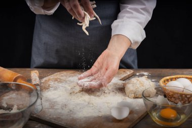 Kadın eli, un ve hamur. Ev yapımı pişirme hamuru pişiren önlüklü bir kadın. Ev yapımı, sade bir atmosfer. Sıradışı ışıklandırması olan karanlık bir arka plan..