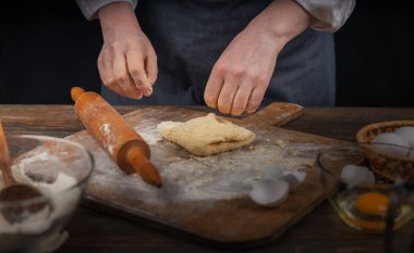 Kadın eli, un ve hamur. Ev yapımı pişirme hamuru pişiren önlüklü bir kadın. Ev yapımı, sade bir atmosfer. Sıradışı ışıklandırması olan karanlık bir arka plan..