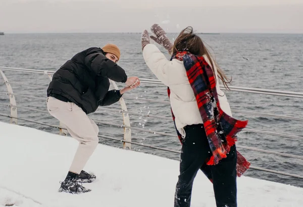 Loving couple play snowballs in winter near the sea