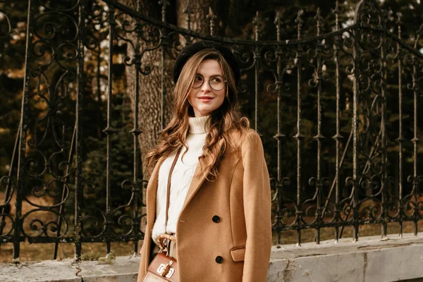 beautiful young woman in beret and coat walks in the autumn city
