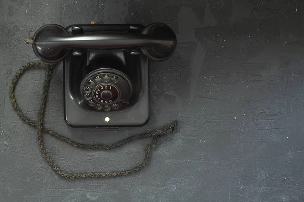 black old telephone receiver hanging on black background with texting space, waiting for phone call, vintage telephone