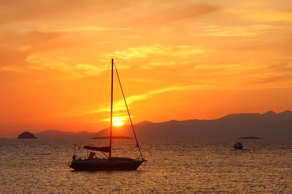 Günbatımında yalnız yelkenli. Turuncu güneşli atmosferik deniz manzarası.