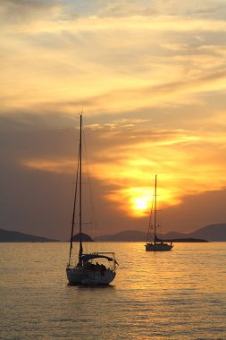 Günbatımında yalnız yelkenli. Turuncu güneşli atmosferik deniz manzarası.