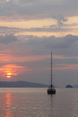Günbatımında yalnız yelkenli. Turuncu güneşli atmosferik deniz manzarası.