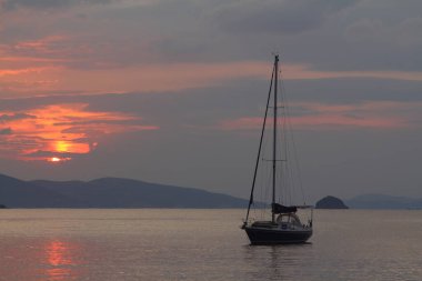 Günbatımında yalnız yelkenli. Turuncu güneşli atmosferik deniz manzarası.