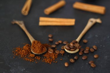 Siyah arka planda iki kaşık kahve. Kahve çekirdekli bir kaşık. Kahveli ikinci kaşık. Yakınlarda kahve çekirdeği var.