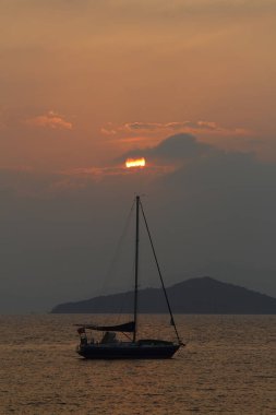 Günbatımında yalnız yelkenli. Turuncu güneşli atmosferik deniz manzarası.
