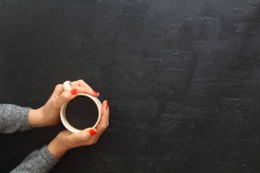 Kırsal ahşap masa zemininde kahve bardaklarını tutan kadın eller, bir kadının elleri, bir fincan sert kahveyi ahşap masada tutuyor. Fotokopi alanı olan kahve fanı üst görünümü.