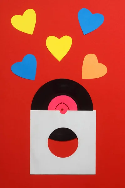 Aged paper cover and vinyl LP record isolated on Red background. 45rpm Vinyl Record with Sleeve. With Colorful hearts.