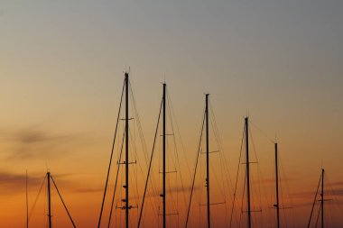 Mavi gökyüzünde, gün batımında, yelkenli teknelerinin direkleri arasında alevli zıt bulutlar..