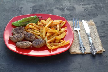 Kırmızı tabakta siyah arka planda köfteler ve patatesler.