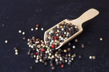 Ahşap arka planda ahşap kaşıkta renkli biber taneleri.