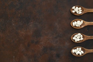 Ahşap arka planda izole edilmiş tahta kaşıkta beyaz böbrek fasulyesi. Üst Manzara. Düz yatıyordu