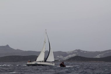 Bodrum, Türkiye. 10 Şubat 2018: Ünlü tatil beldesi Bodrum 'un kıyılarında, Ege Denizi' nin mavi sularında rüzgarlı havada yelken açan yelkenliler.