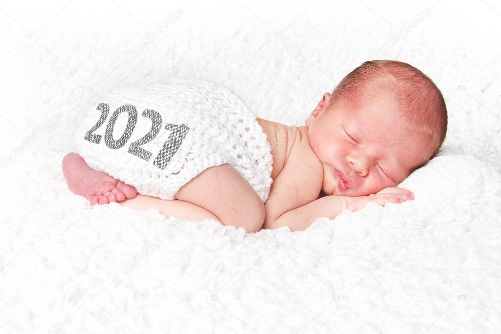 Newborn baby asleep on a white blanket with 2021on his knitted diaper cover. Happy New Year baby.  