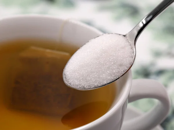 Zbliżenie łyżeczki srebra z białym cukrem nad filiżanką herbaty — Zdjęcie stockowe