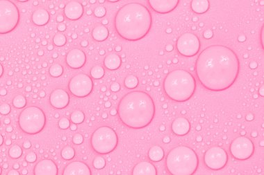 Su damlaları pembe arka plan dokusuna düşer. Arkaplan camı su damlalarıyla kaplı. Suda kırmızı kabarcıklar.