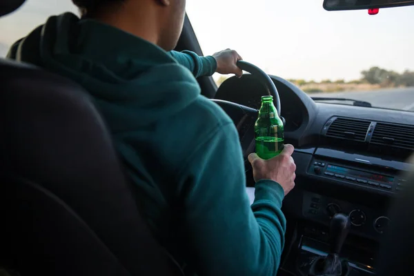 Drunk young man drives a car with a bottle of beer. This is a campaign picture of \
