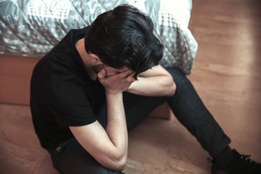 Genç üzgün adam odada oturuyor.