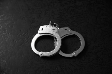 Kara masanın arkasına kelepçelenmiş.