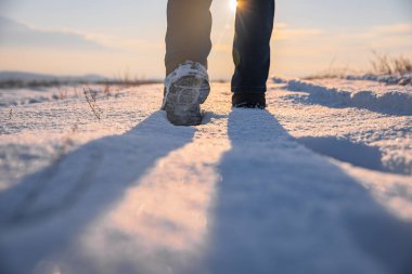 Adam güneşin altında karda yürüyor.
