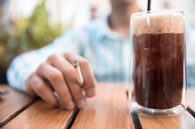 Bir adam sokak kafeteryasında oturup sigara içiyor.