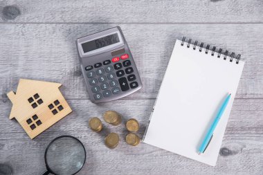 tablo üzerinde hesap makinesi ve defter olan ev modeli ve madeni paralar
