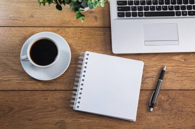 Dizüstü bilgisayarı, kahve fincanı ve not defteri olan ofis masası.