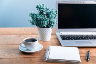 Not defterli bilgisayar ve ofislerinde çiçekler olan bir fincan kahve.