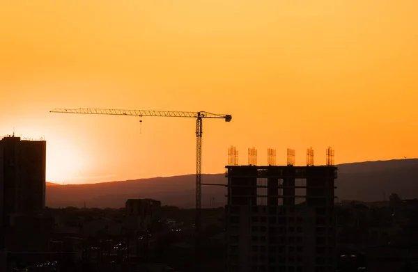 Construction site at sunrise. Industrial construction cranes and building silhouettes over sun at sunris