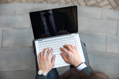 İşadamı bilgisayarda çalışıyor, merdivenlerde oturuyor.