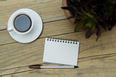 Tahta arka planda bir fincan kahve, kağıt ve kalem.