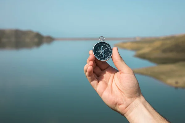 man hand holding compass in lake backgroun